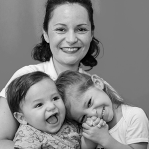 Retrato preto e branco da Natália Públio com seu filho e sua filha no colo